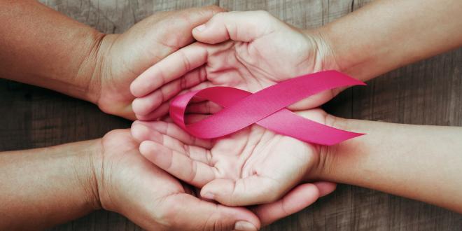 A larger pair of hands cupping a smaller pair of hands palms up with a pink breast cancer awareness ribbon.