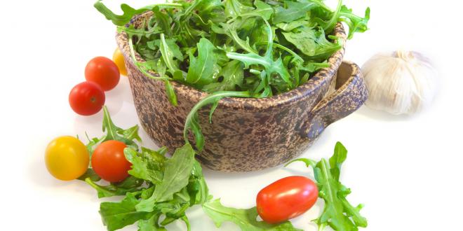 Bowl of arugula with cherry tomatoes and a bulb of garlic surrounding the bowl